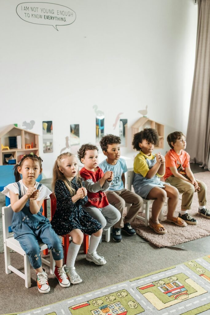 Children sitting together in a bright kindergarten classroom with toys and playful decor.
